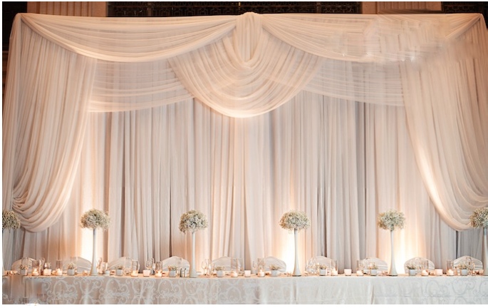Elegant ivory draped backdrop behind a candlelit head table